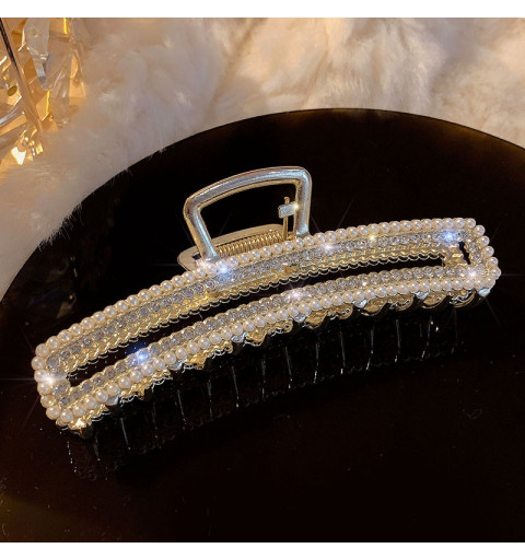 Hårklämma i guldig metall med utskärning och en dekorativ kant av glasstenar och en dekorativ kant av pärlor.